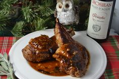 two pieces of meat on a plate next to a bottle of wine and an owl figurine