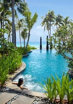 a woman laying on the edge of a swimming pool surrounded by palm trees and water