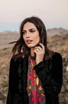 a woman standing in the desert with her hand on her chin and looking off into the distance