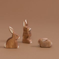 three wooden rabbits sitting next to each other on top of a brown surface with one rabbit looking at the camera