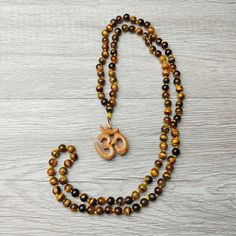 37" Unique Handcrafted Top Quality Tiger Eye Regal Beaded Knotted Necklace with Sandalwood Om Carved Scared Symbol. Sacred Amulet, Protection and Blessing Jewelry Gift. Handcrafted, Comes with A Velvet Pouch. ✥ Mala Necklace: 37" Long - 8mm beads ❀❀❀ Please look closely at photos as part of item description, the product in the images is as the one you will receive and is sold "as is". Please review the description and images prior to purchasing to ensure this item meets your satisfaction. We wel Adjustable Brown Mala For Festival, Brown 8mm Beads Mala For Festival, Brown Beaded Necklace With 108 Beads For Festivals, Brown Beaded Mala For Festivals, Brown Mala With 8mm Beads For Festival, Brown Beaded Necklace For Festivals, Brown Wooden Beads For Festivals, Festival Brown Beaded Mala, Bohemian Brown Mala For Festivals