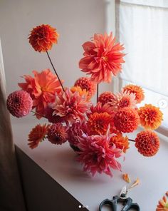 an arrangement of flowers in a vase on a window sill next to some scissors