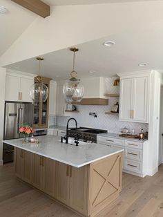 a kitchen with white cabinets and marble counter tops, an island in the middle is surrounded by wood flooring