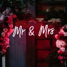 the words mr and mrs are lit up in front of a doorway decorated with flowers