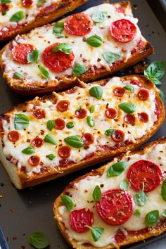 four slices of bread with tomatoes and basil on top, sitting on a baking sheet