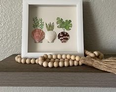 three seashells are mounted in a white frame on a shelf next to a beaded necklace