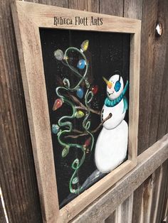 a painting of a snowman is hanging on the side of a wooden fence with words written below it