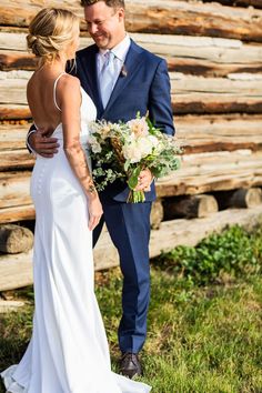 a bride and groom standing in front of a log cabin