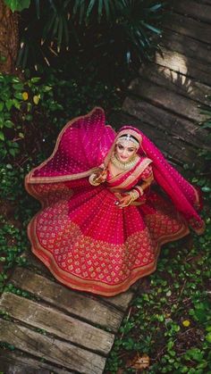 a woman in a red and pink outfit is sitting on a wooden walkway near some plants