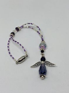 a purple beaded necklace with an angel charm hanging from it's side on a white surface