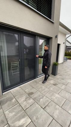 a man in black jacket and boots leaning on glass door to open the sliding doors