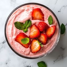 there is a glass with some strawberries in it and mint leaves on the side