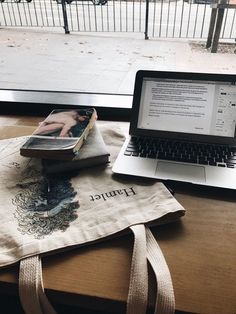 an open laptop computer sitting on top of a wooden table next to a book bag