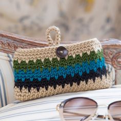 a crocheted purse sitting on top of a white chair next to some sunglasses