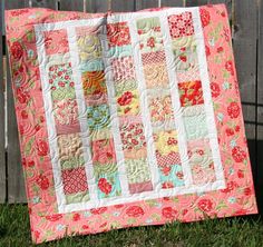 a quilted blanket sitting on the grass next to a fence