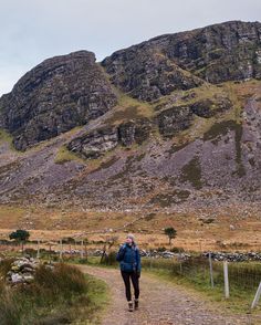 a person walking down a dirt road in front of some mountain side hills and rocks