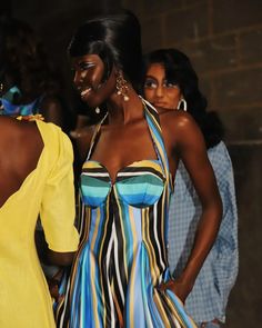 two women in dresses standing next to each other at a fashion show with one woman wearing a yellow dress