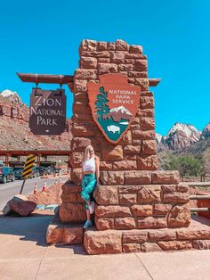 a woman sitting on top of a sign at the entrance to national park in arizona