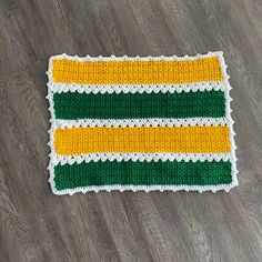 a green, yellow and white crocheted rug on a wooden floor