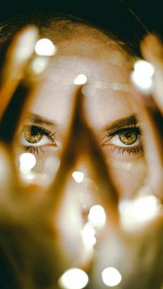 a woman's eyes are reflected in the reflection of her hands with lights on them