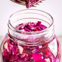 a jar filled with red cabbage sitting on top of a table next to a spoon