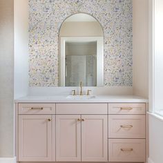 a bathroom vanity with two sinks and a large mirror above it, in front of a floral wallpaper