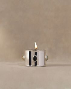 a small silver candle holder with a black and white stripe design on the front, holding a single lit candle