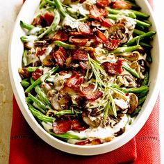 a white dish filled with green beans, bacon and mushrooms on top of a red towel