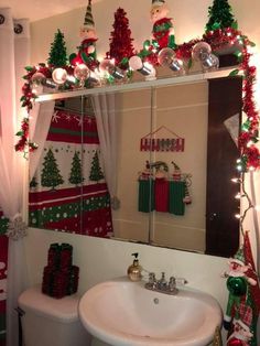 a bathroom decorated for christmas with red and green decorations on the wall, white toilet and sink