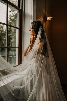 a woman is looking out the window wearing a wedding veil and holding her hand to her face