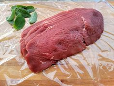 a piece of meat sitting on top of a plastic wrapper next to some leaves