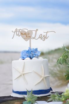 a white wedding cake with blue flowers and starfish on the top that says at least