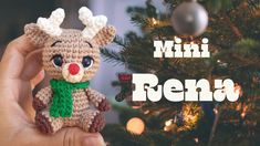 a hand holding a small crocheted reindeer ornament in front of a christmas tree