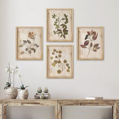 four framed pictures on the wall above a table with vases and flowers in them