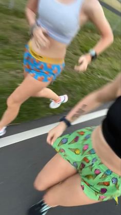 two women are running on the street in shorts and sports bras, one is holding her leg up