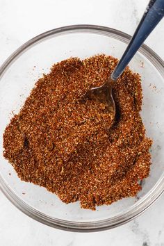 a glass bowl filled with spices on top of a white counter next to a metal spoon