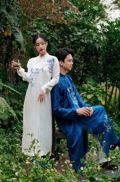 a man and woman sitting on a bench in the woods, dressed in traditional chinese clothing