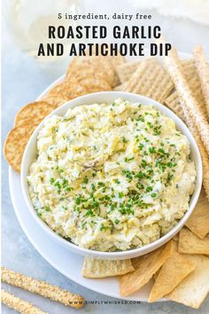 a white bowl filled with garlic and artichoke dip surrounded by crackers on the side