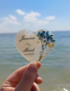 a person holding up a heart shaped piece with flowers on it in front of the ocean