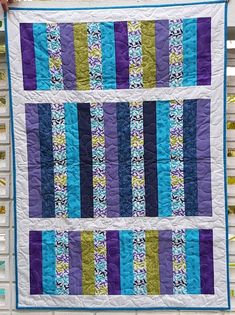 a quilted wall hanging on the side of a building with blue, green and purple strips