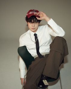 a young man sitting in a chair wearing a hat and tie with his hands on his head