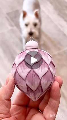 a hand holding a pink ornament with a dog in the background