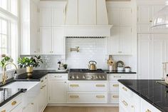 a white kitchen with black counter tops and gold trim on the cabinets is pictured in this image