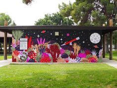 a colorful mural on the side of a building with trees and grass in front of it