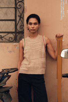 a woman leaning against a wall with her hand on the back of a scooter