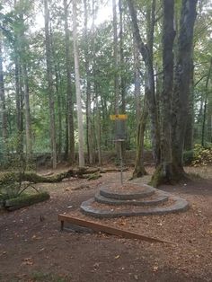 a wooden bench sitting in the middle of a forest next to a tall tree with a yellow sign on it