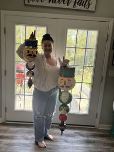 a woman standing in front of a door holding two decorative objects with faces on them