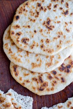 four pita breads on a wooden surface next to some pieces of white bread