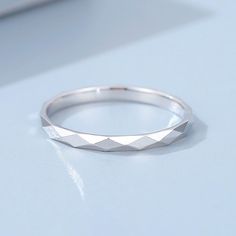 a white gold wedding band on a blue surface with a diamond cut design in the middle