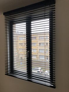 a window with black blinds in front of it and some cars parked outside the window